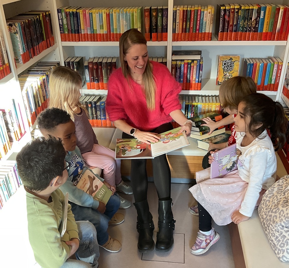 Eine Mutter liest Kindern vor, sie sitzen in der Mediathek von Büchern umgeben