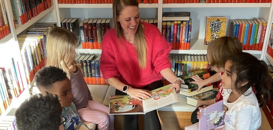 Eine Mutter liest Kindern vor, sie sitzen in der Mediathek von Büchern umgeben