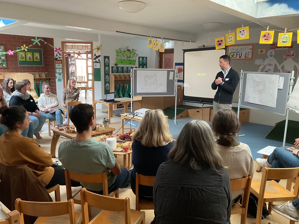 Blick aus dem Publikum nach vorne, wo Thomas Speth das Publikum begrüßt