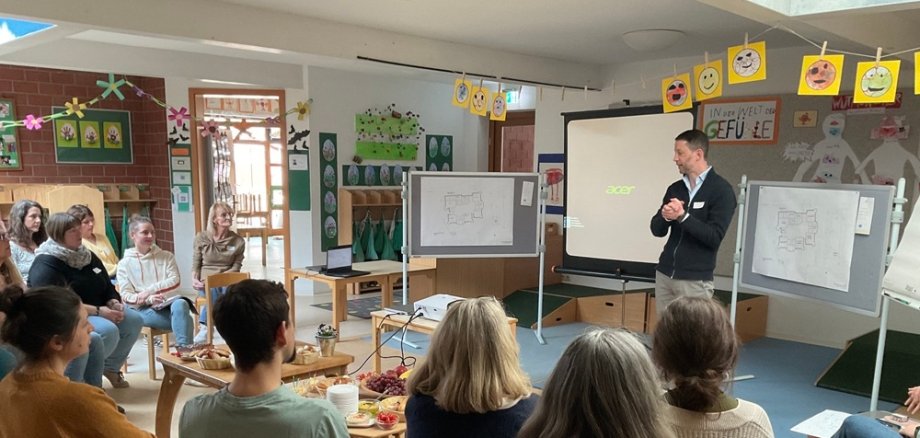 Blick aus dem Publikum nach vorne, wo Thomas Speth das Publikum begrüßt