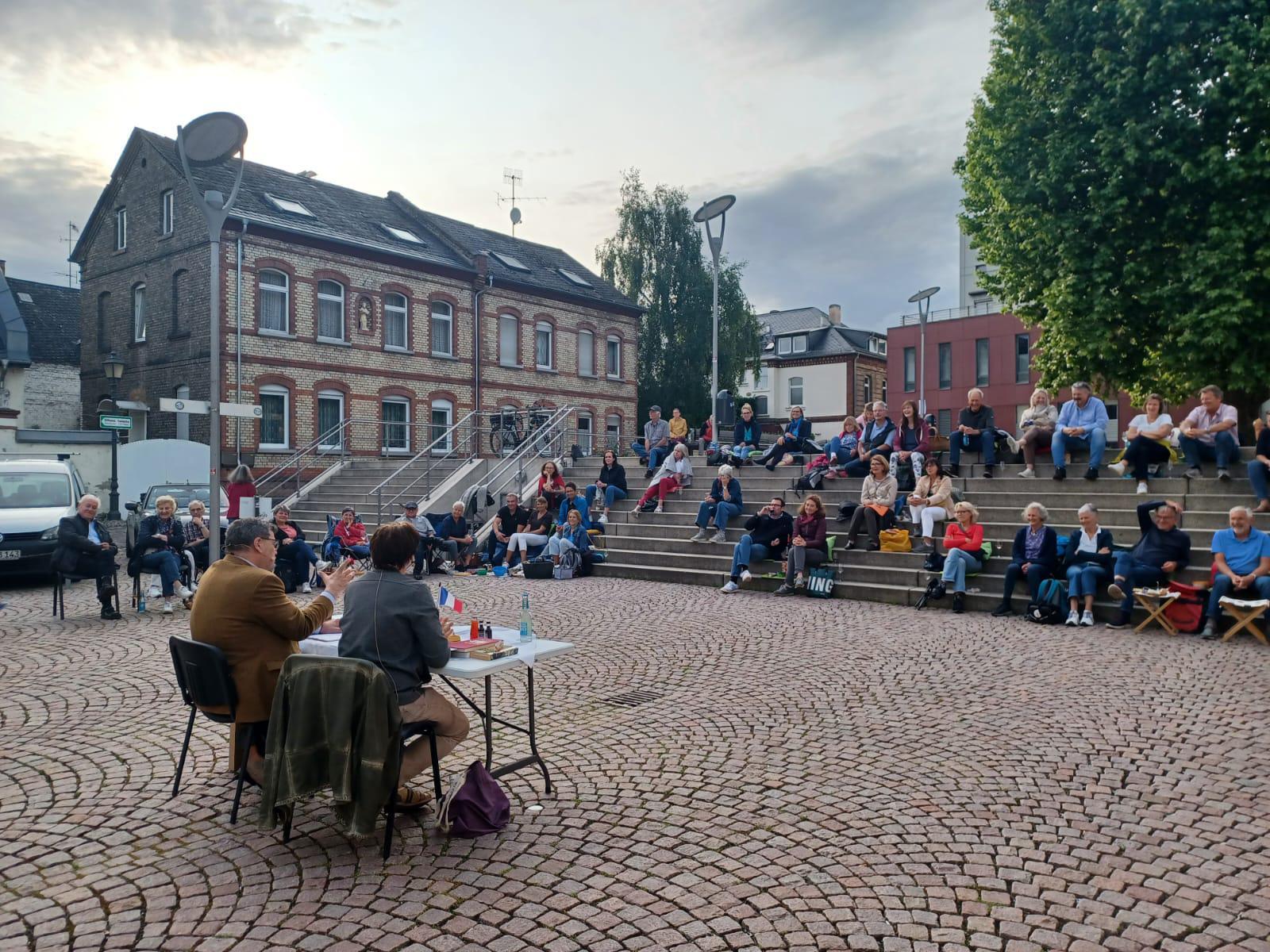 Besucher auf dem Platz der Deutschen Einheit auf Stufen sitzend, hören Les Croque Messieurs zu
