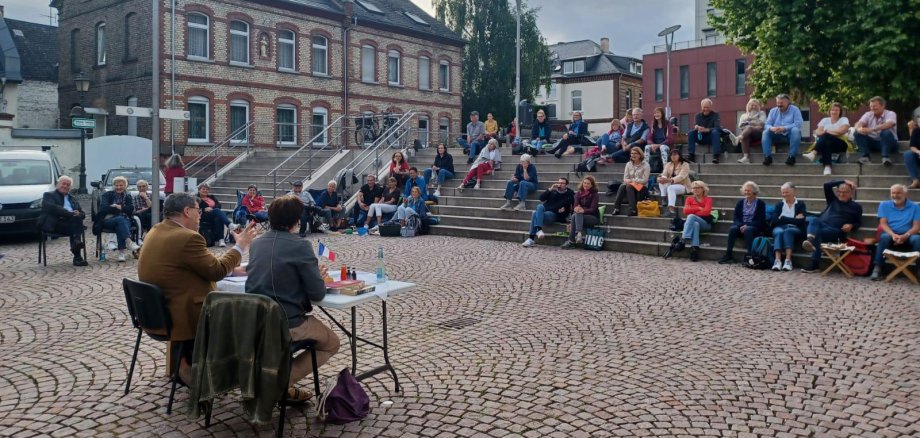 Besucher auf dem Platz der Deutschen Einheit auf Stufen sitzend, hören Les Croque Messieurs zu