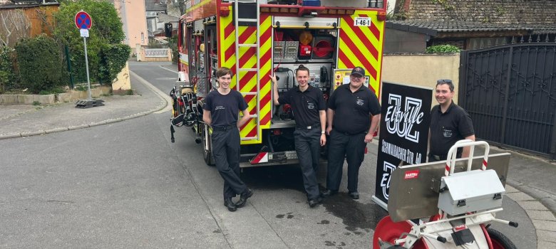 Vier junge Feuerwehrmänner mit Feuerwehrfahrzeug
