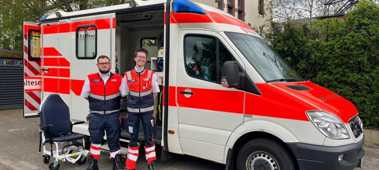Zwei Mitarbeitende der Malteser mit Rettungsfahrzeug