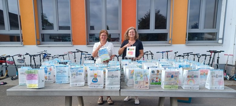 Bunte Lesetüten stehen auf einem Tisch, dahinter Bettina Lauer und Petra Bungert