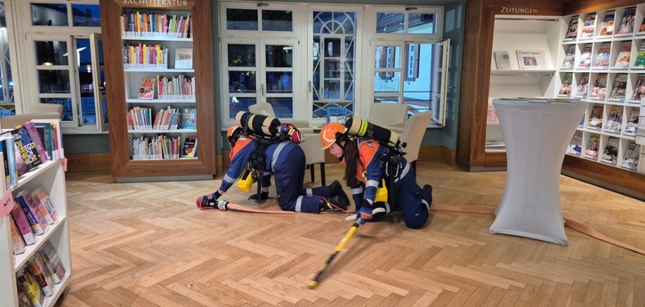 Zwei junge Feuerwehrleute kriechen über den Boden im Lesesaal
